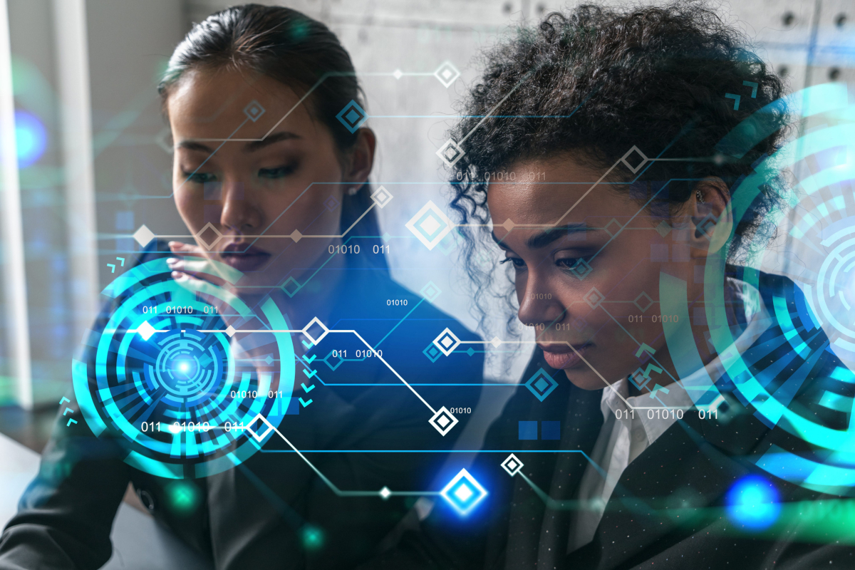 Two female professionals looking intently at a digital overlay of holographic circuits, data streams, and binary code interfaces.