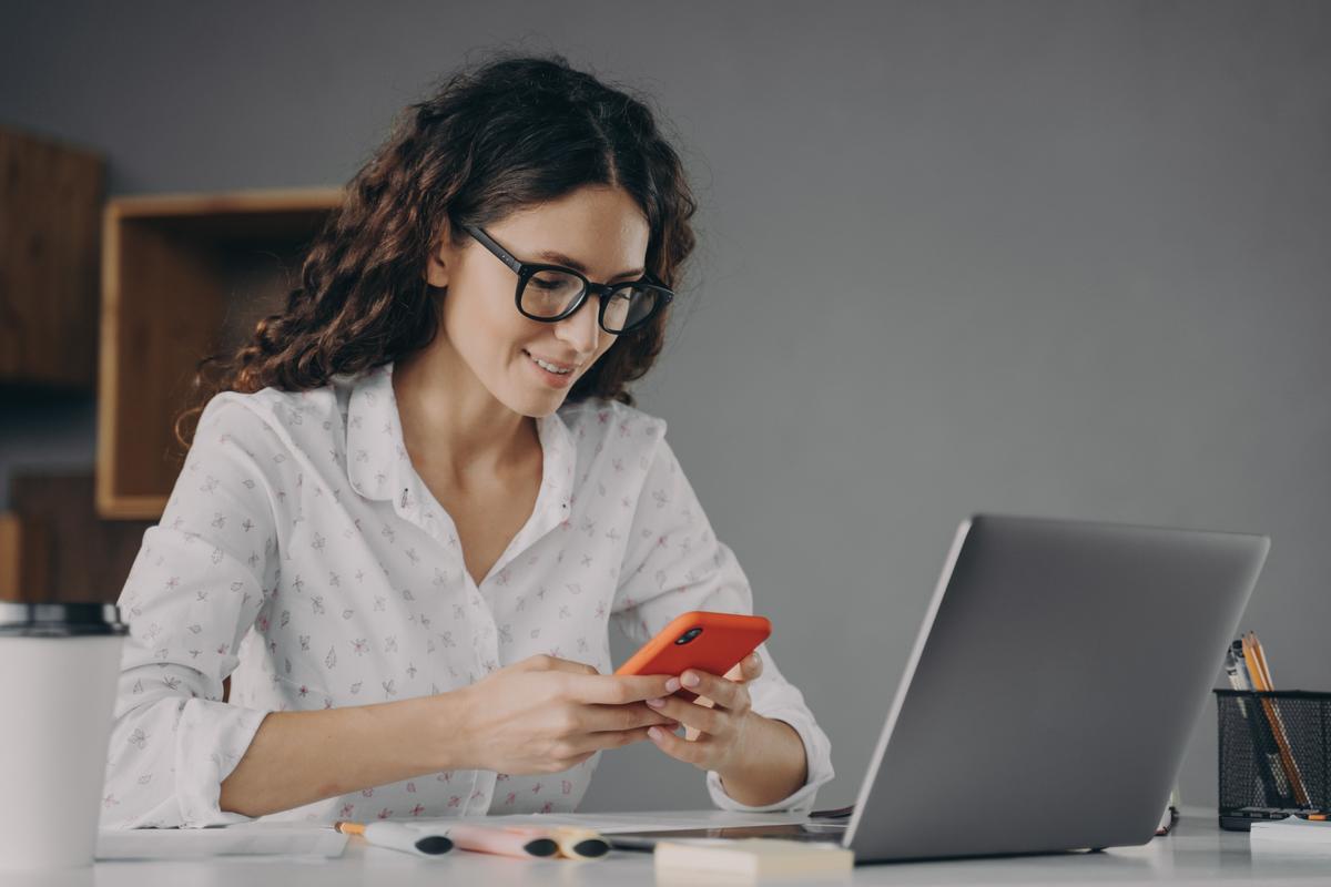 Woman in front of a laptop looking at mobile phone