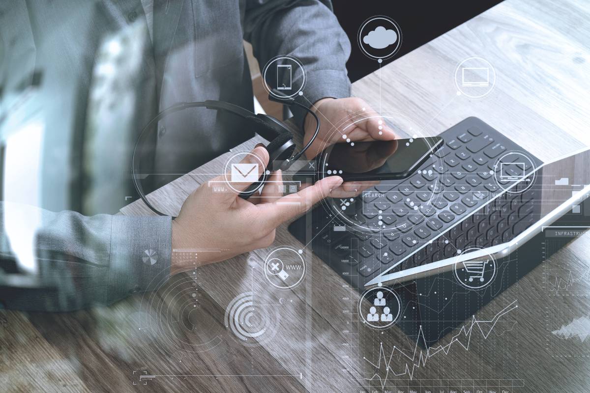 Man holding headphones while using mobile phone and laptop