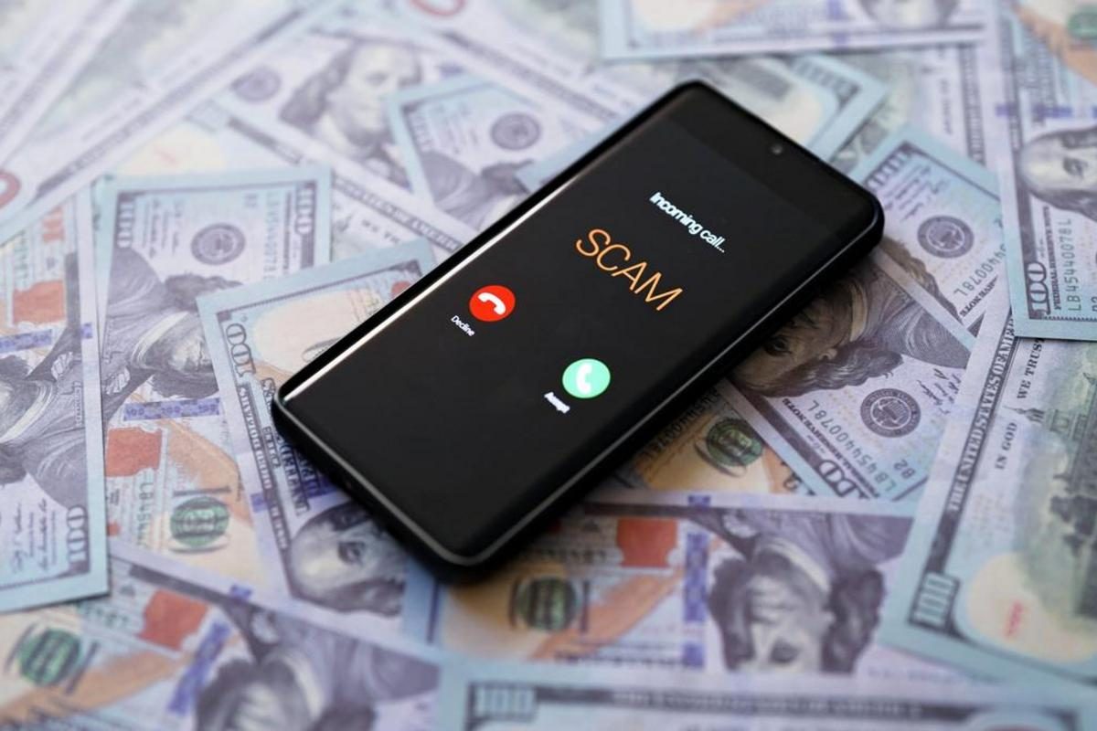 Smartphone showing an incoming call labeled SCAM on a pile of hundred-dollar bills.
